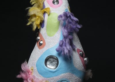 A white irregular shaped sculpture with bright patches and featured colorful hair.