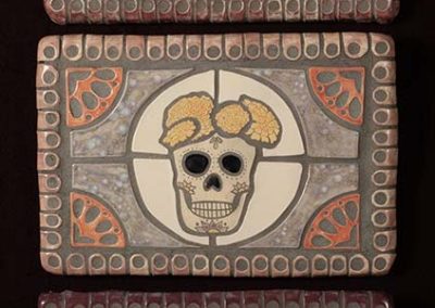 Three ceramic pieces depicting skulls and flowers for Día de los Muertos .