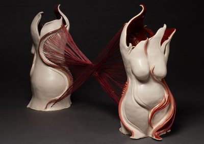 Two center-body sculptures of a woman with red string attached to the back like a corset and attaching it to the other body.