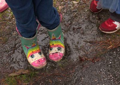 An image of a kids unicorn rainboots as they splash in a mud puddle.