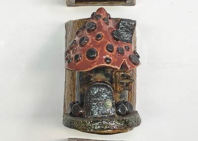 Three semi-hallow sculptures of tree bark, one with slugs, one with a gnome house, and one with red eyes.
