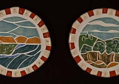 Two circular sculpture ceramics of landscapes - one of mountains and see and the other of hills and trees with the text "From the river to the sea" on one and "Palestine will be free" on the other.