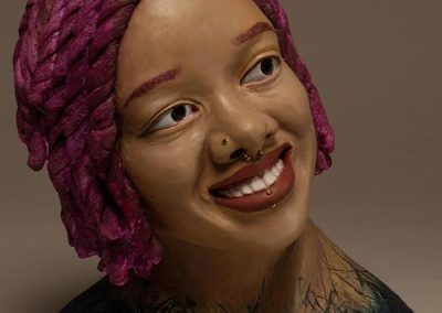A ceramic sculpture of a person with purple hair, a nosering, lip ring, and blue shoulders smiling.