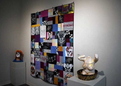A quilt on the wall and two sculptures on either side.