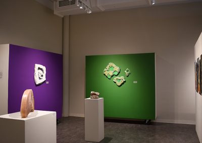 A purple wall and a green wall with artwork on them and sculptures on pedestals in the middle of the room.