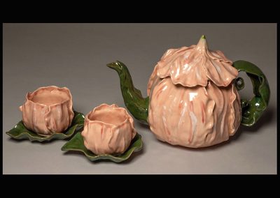 A handmade tea set with a nature theme as if the main parts are made of a pink flower and the handles, plates, and spout are stems or leaves.